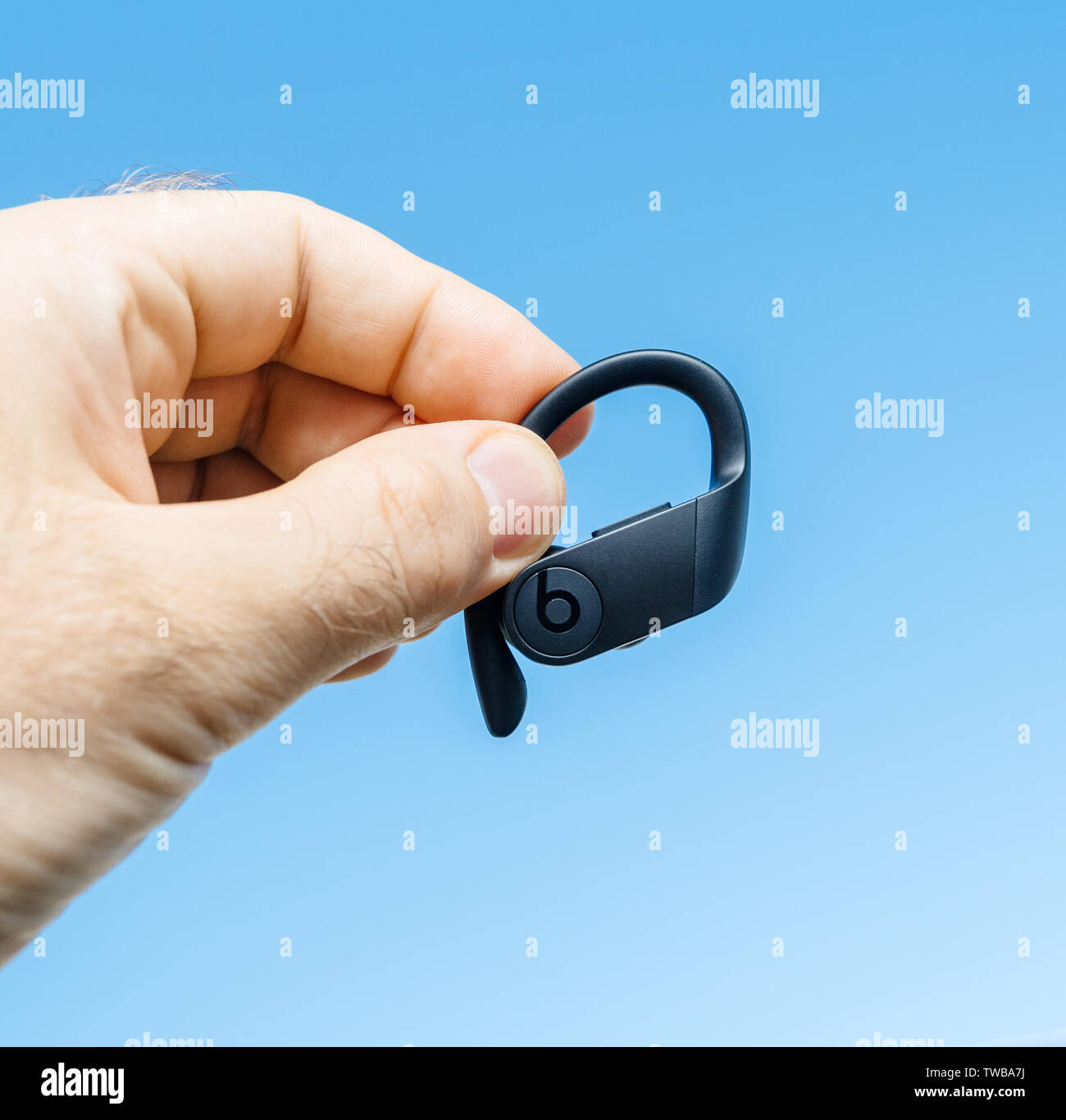 Paris, France - Jun 17, 2019: Close-up of man hand holding demonstrating new Powerbeats Pro Beats by Dr Dre wireless high-performance earphone with integrated Siri - blue sky square image Stock Photo
