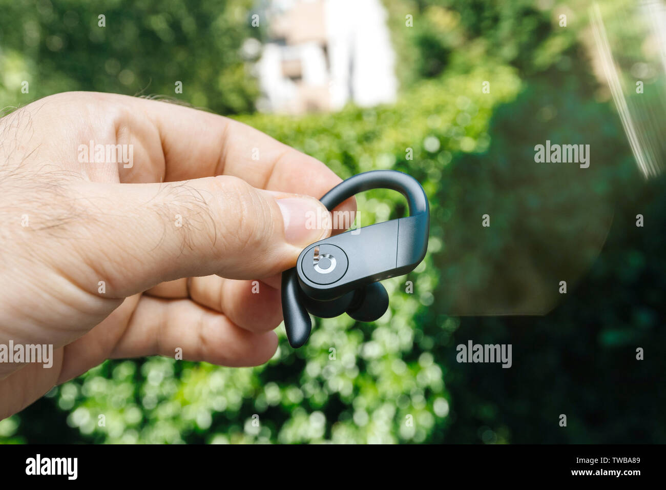 Paris, France - Jun 17, 2019: Close-up of man hand holding new Powerbeats Pro Beats by Dr Dre wireless high-performance earphone with integrated Siri - green park forest background Stock Photo