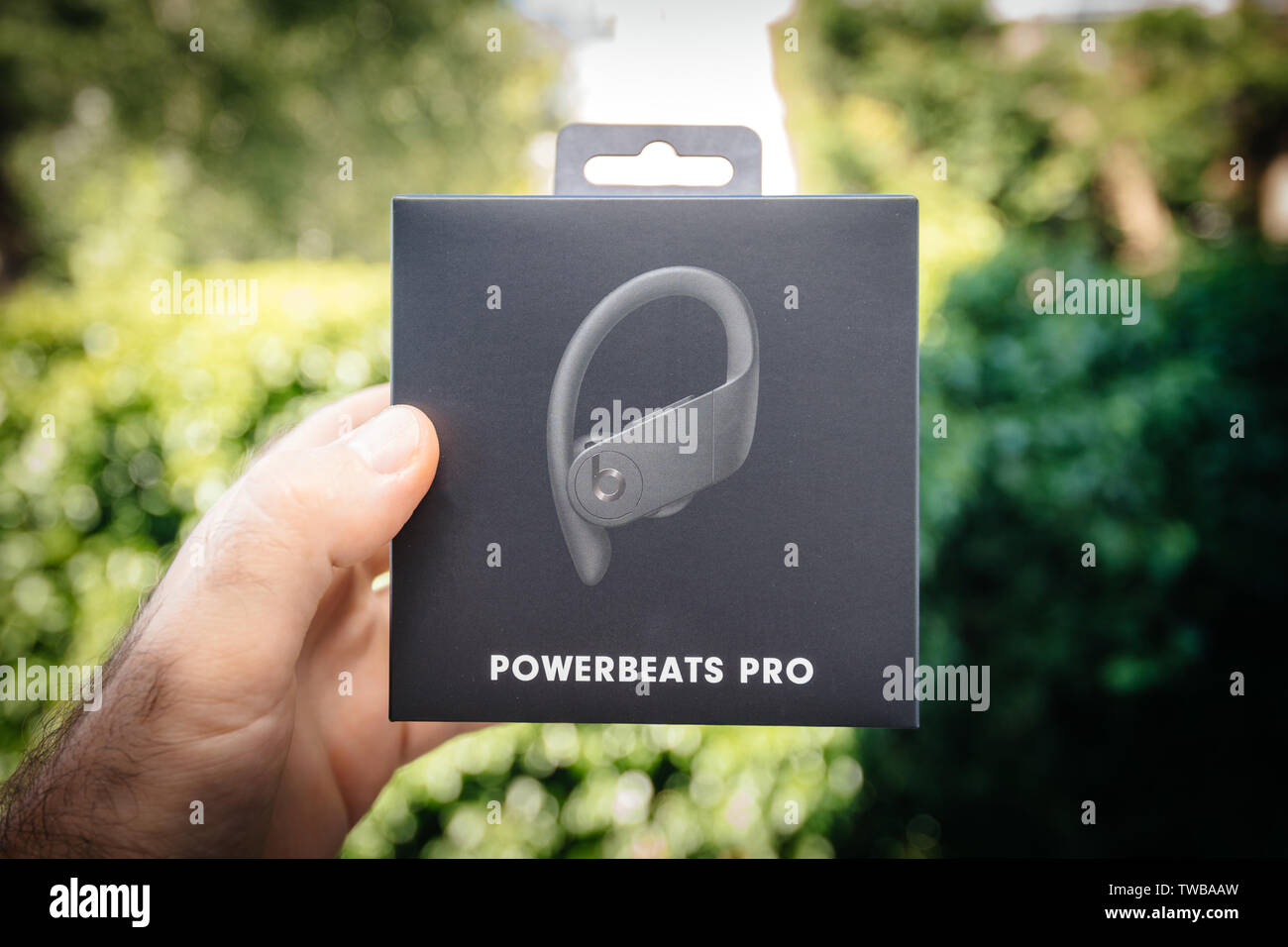 Paris, France - Jun 17, 2019: Man hand holding against green park background Powerbeats Pro Beats by Dr Dre wireless high-performance earphones waterproof and workout professional headphones Stock Photo