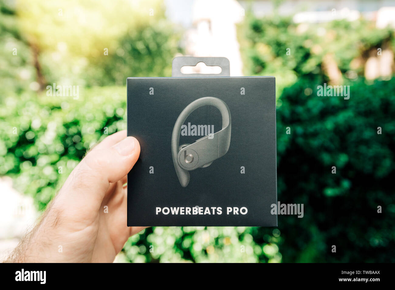 Paris, France - Jun 17, 2019: Man hand holding against green park background Powerbeats Pro Beats by Dr Dre wireless high-performance earphones waterproof and workout professional headphones Stock Photo