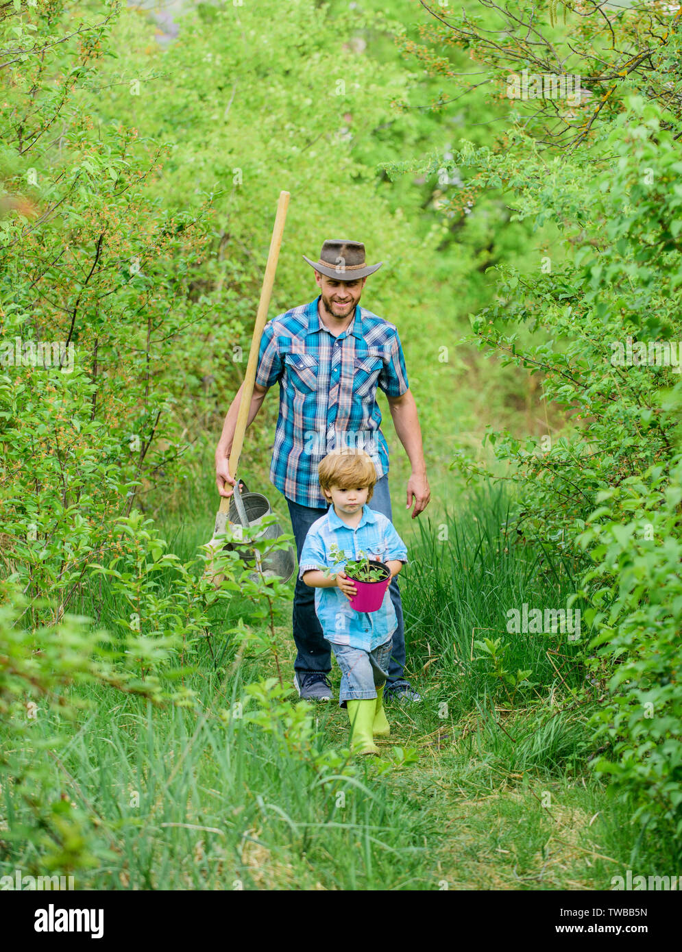 Little helper in garden. Planting flowers. Growing plants. Boy and father in nature with watering can and shovel. Dad teaching son care plants. Arbor day. Planting trees. Tree planting tradition. Stock Photo