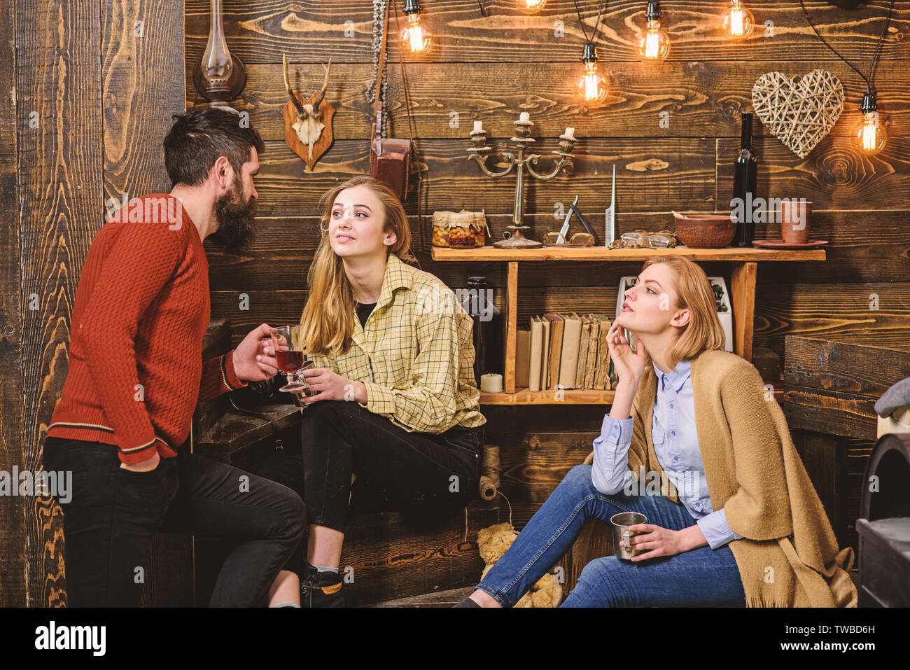 Friends, family spend pleasant evening, interior background. Family enjoy conversation in gamekeepers house. Girls and man on relaxed faces hold metallic mugs, talking. Sincere conversation concept. Stock Photo