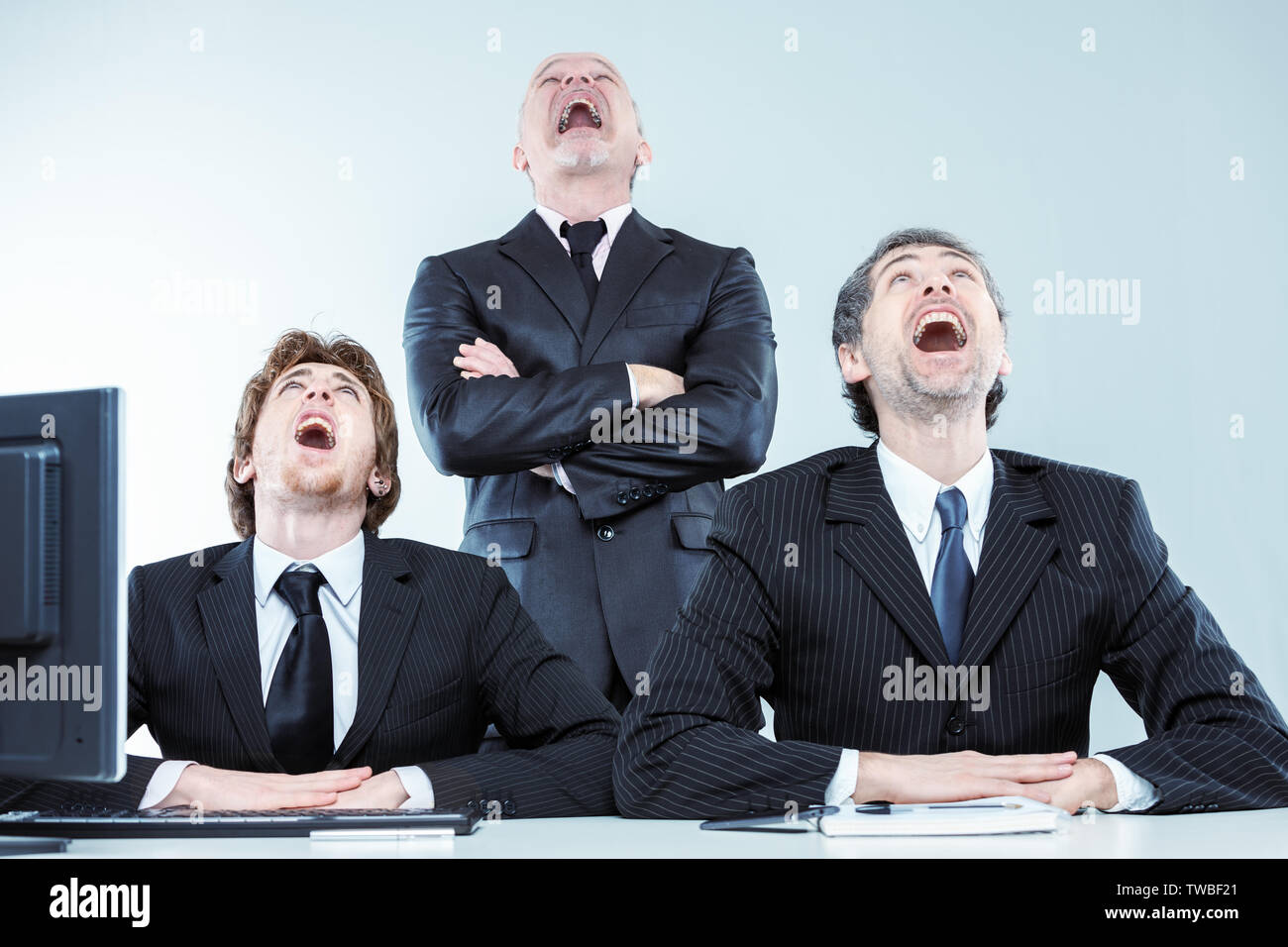 Three businessmen laughing or gawping as they look up at the ceiling in unison with wide open mouths during a meeting Stock Photo