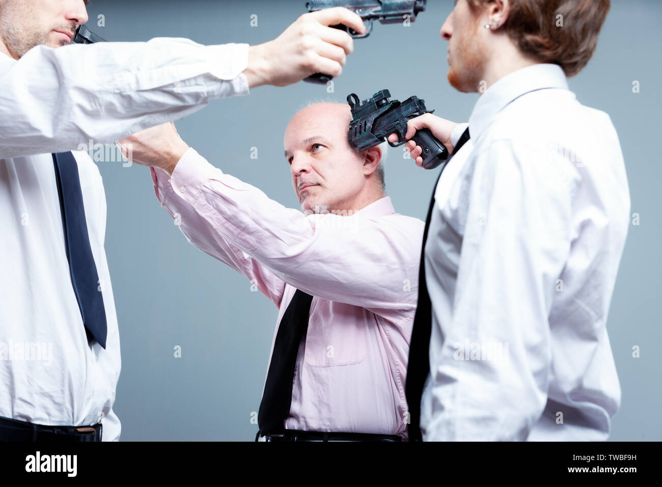 Business stand-off or stalemate concept with three businessman standing in a circle pointing guns at each others heads each determined not to give way Stock Photo