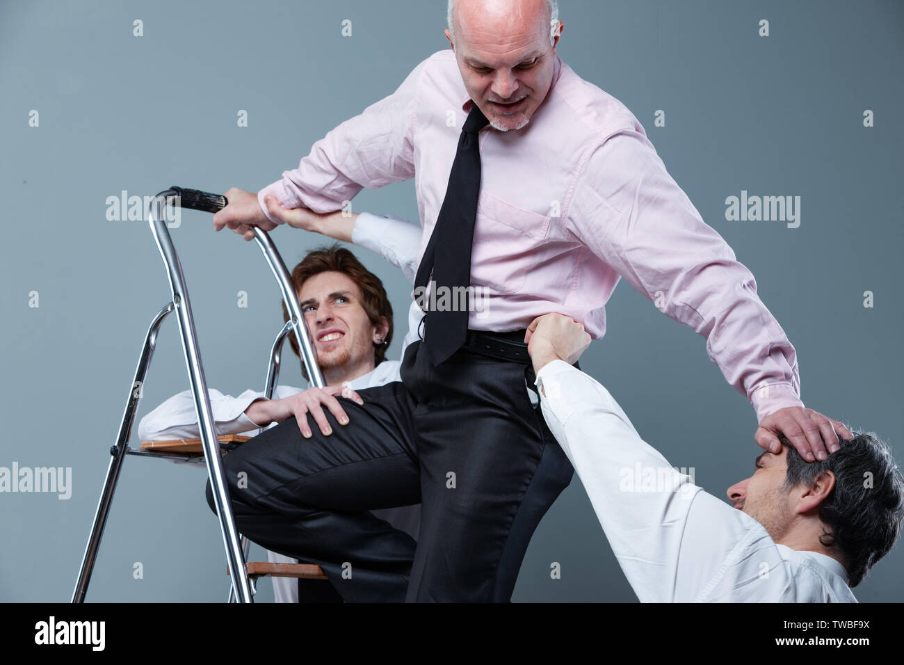 Ambition and climbing the corporate ladder concept with a senior businessman fighting off younger colleagues wishing to displace him from his position Stock Photo