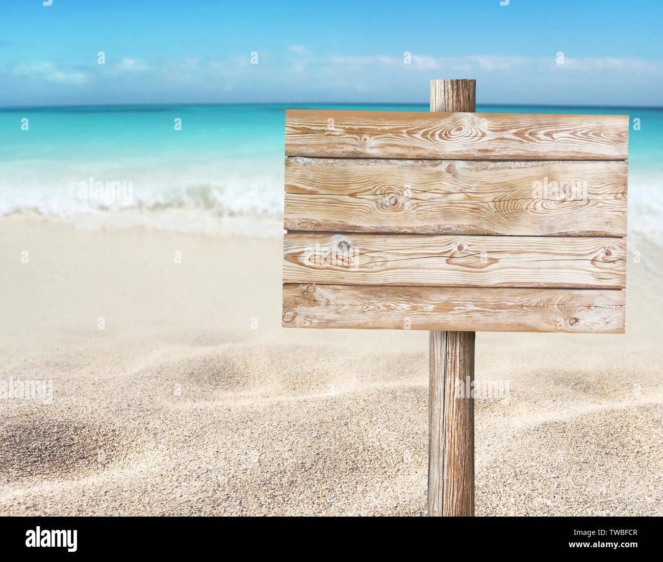 Wooden planks sign board on the beach blurred background.  Tropical island paradise. Sandy shore washing by the wave. Bright turquoise ocean water. Stock Photo