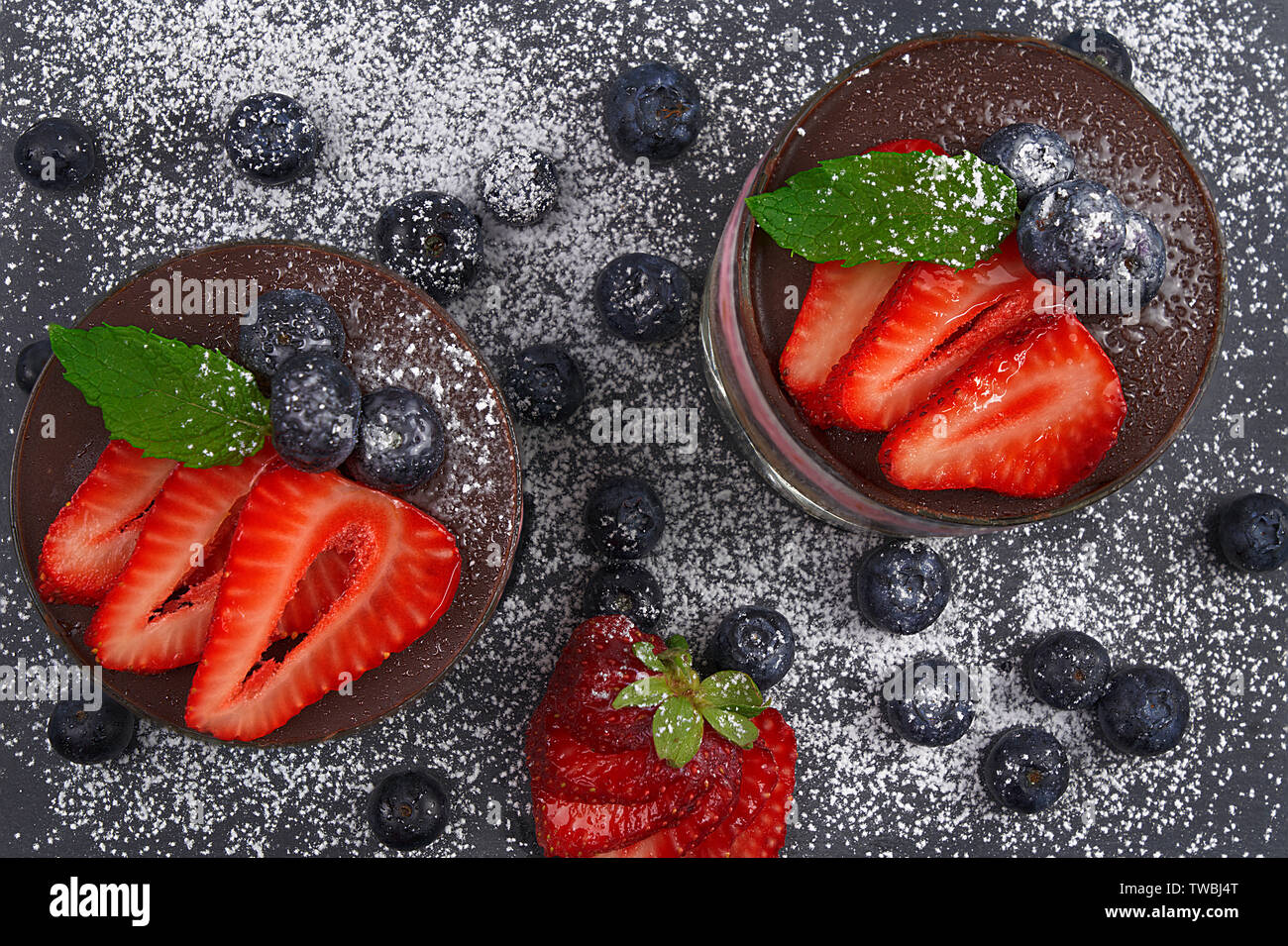 Cherry mousse with crumbled biscuit, cherries in syrup, pineapple cream and chocolate. Decorated with strawberries, blueberries and mint leaves Stock Photo