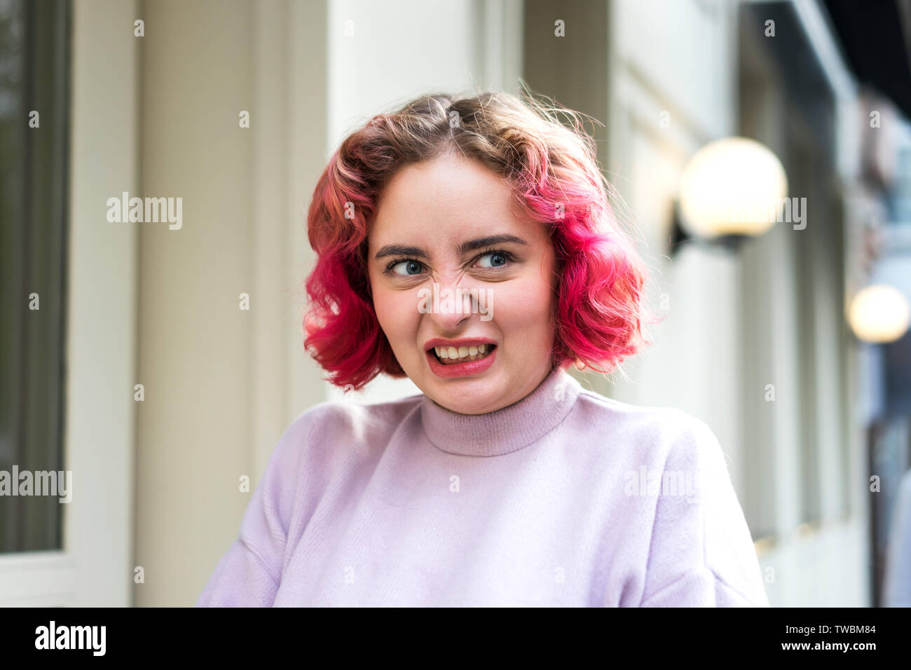 Emotional young woman with pink wavy hair with a grimace of neglect or anger Stock Photo