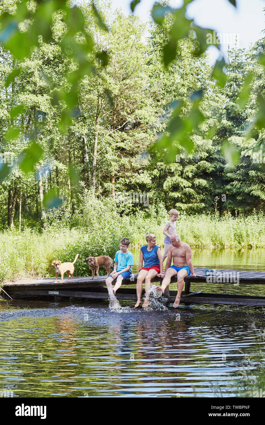 Family spending time together sitting on a bridge over a lake, among the trees, close to nature, during summer vacations. Candid people, real moments, Stock Photo