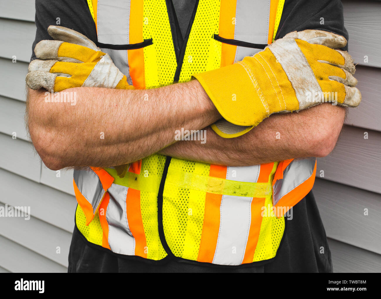 Man wearing safety vest and work gloves beside exterior siding. Stock Photo