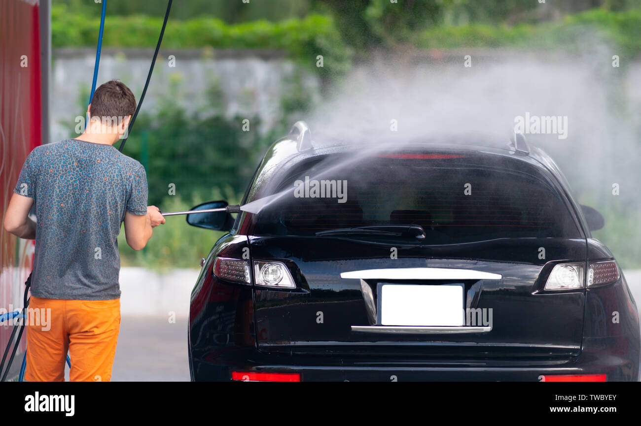 Young man spraying down his car with soapy water while cleaning it at a