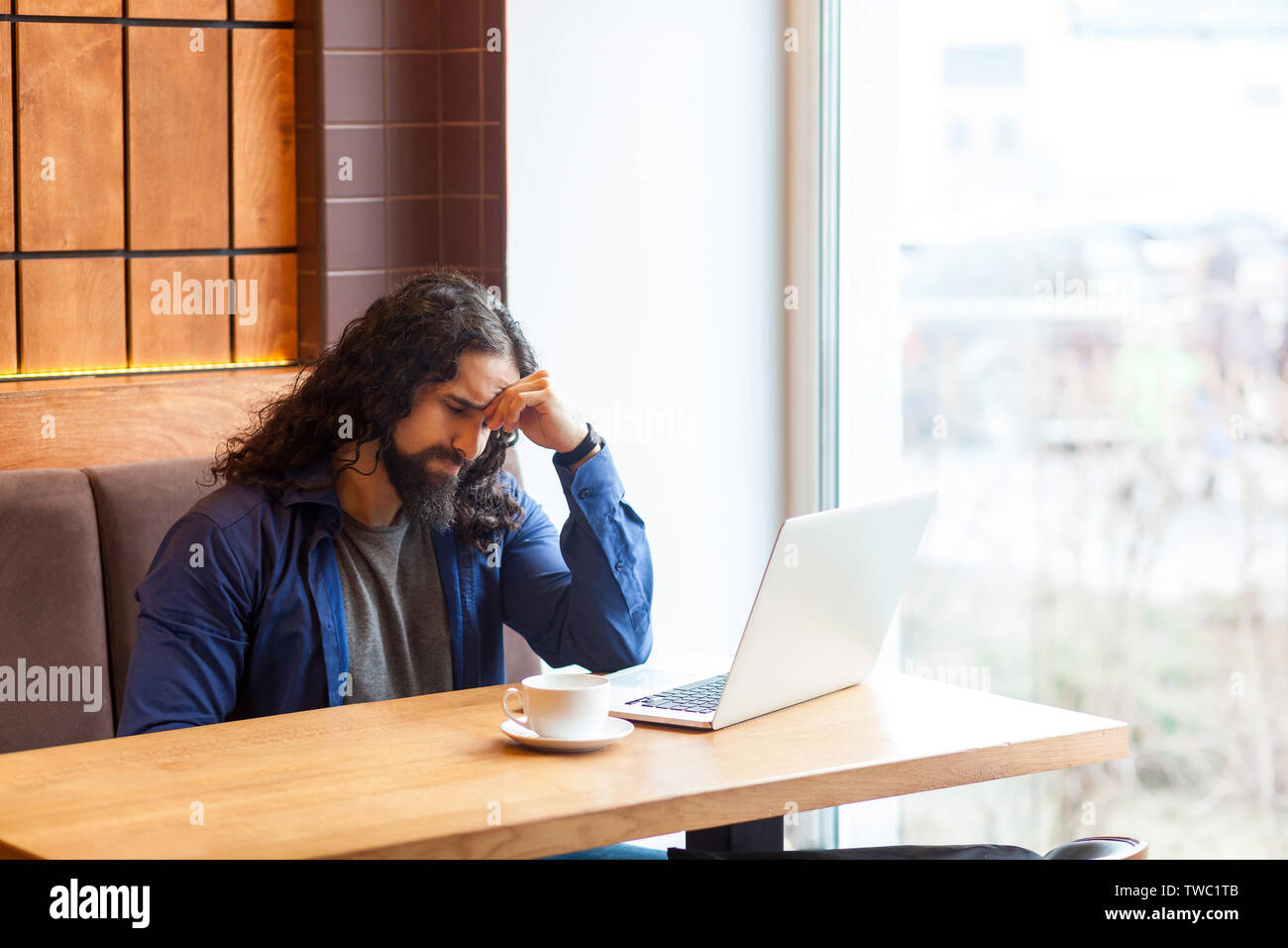 Portrait of tired thoughtful handsome young adult man freelancer in casual style sitting in cafe with laptop, trying to concentrate and remember some Stock Photo