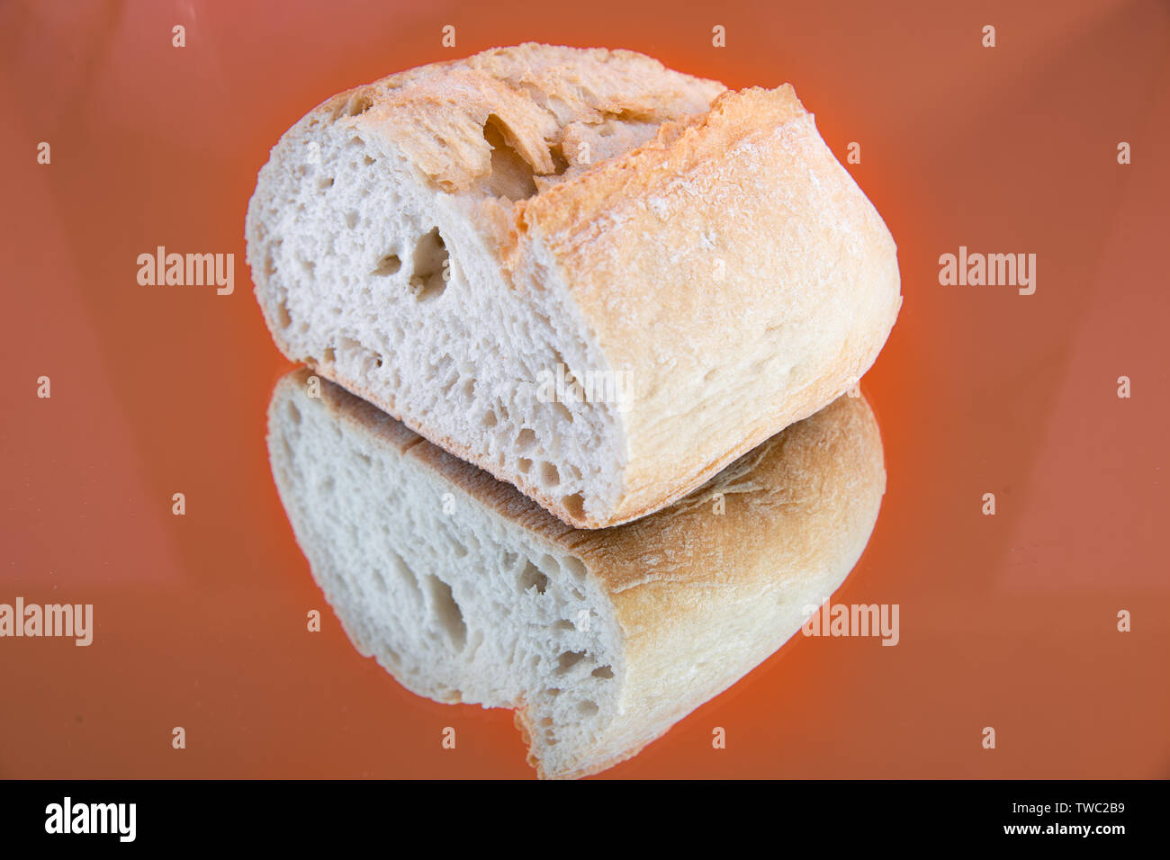 Close-up of a delicious and fresh slice of baguette, on a mirror, isolated in an orange background. Stock Photo