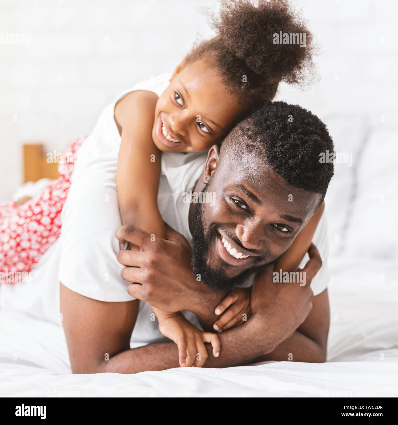 Sincere kid love. Adorable little african girl hugging her daddy, lying