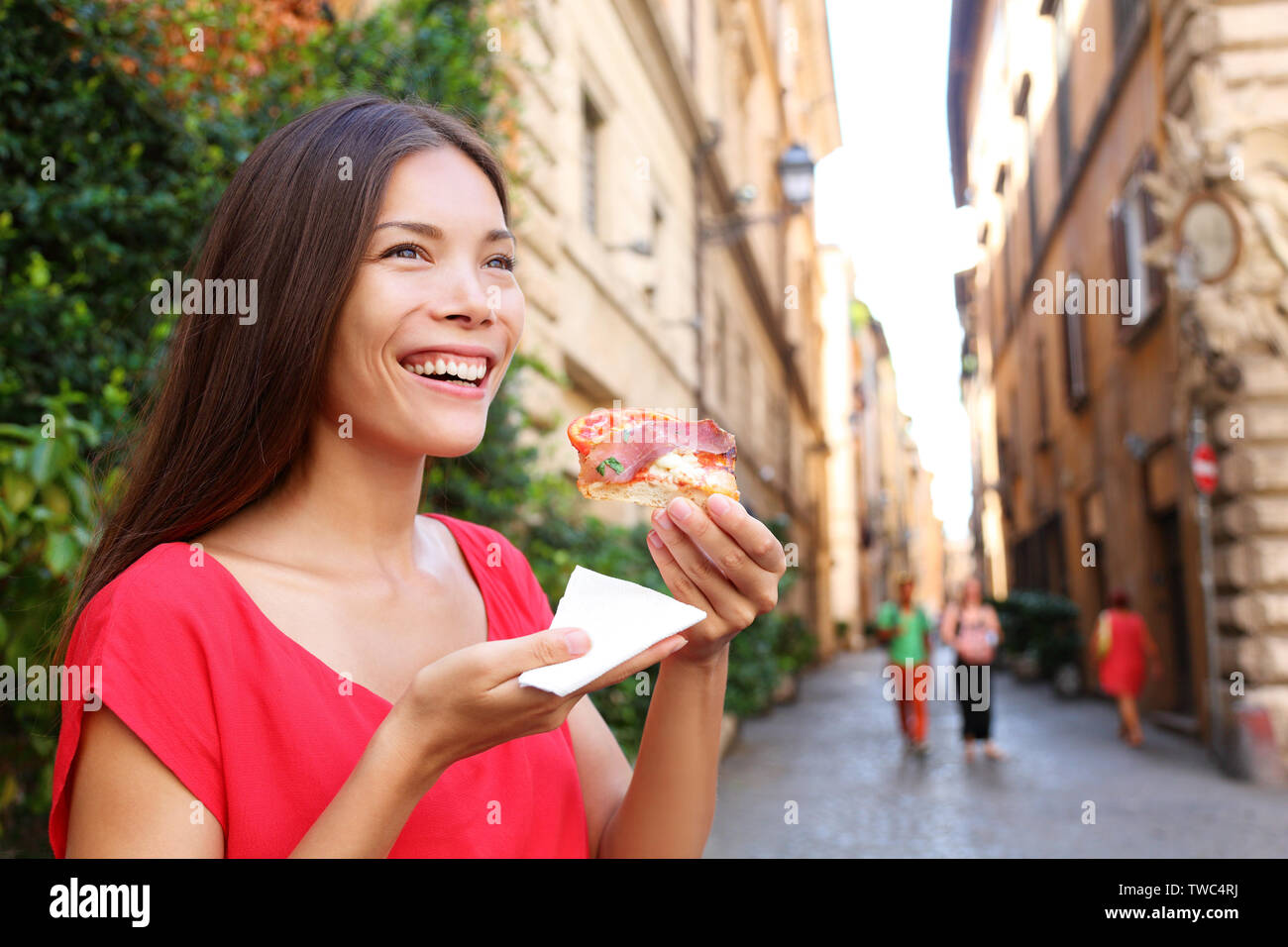 Pizza woman eating pizza slice in Rome, Italy smiling happy outdoors during travel vacation holiday. Beautiful mixed race Asian Caucasian woman enjoying Italian food. Stock Photo