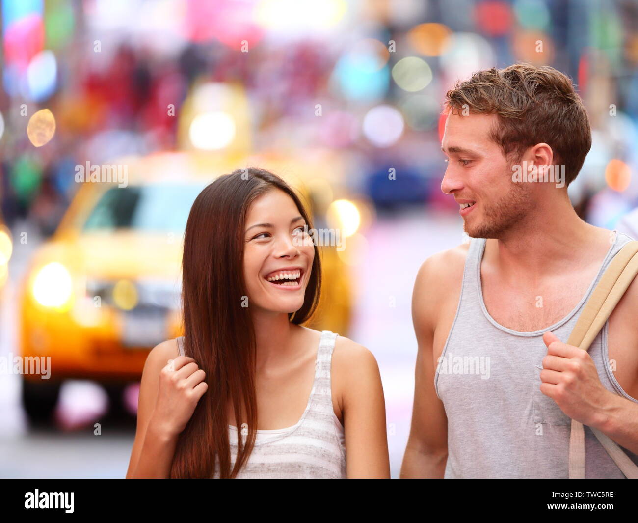People in New York - happy couple on Times Square. Dating young couple in love walking and talking. Beautiful young multiracial tourists on fun date in city, Manhattan, USA. Asian woman, Caucasian man Stock Photo