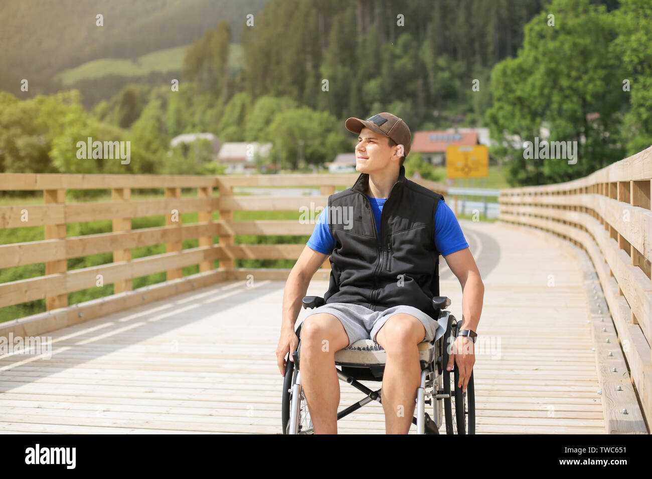 Disabled young man on a wheelchair on a wooden bridge path enjoying in nature looking at beautiful view Stock Photo