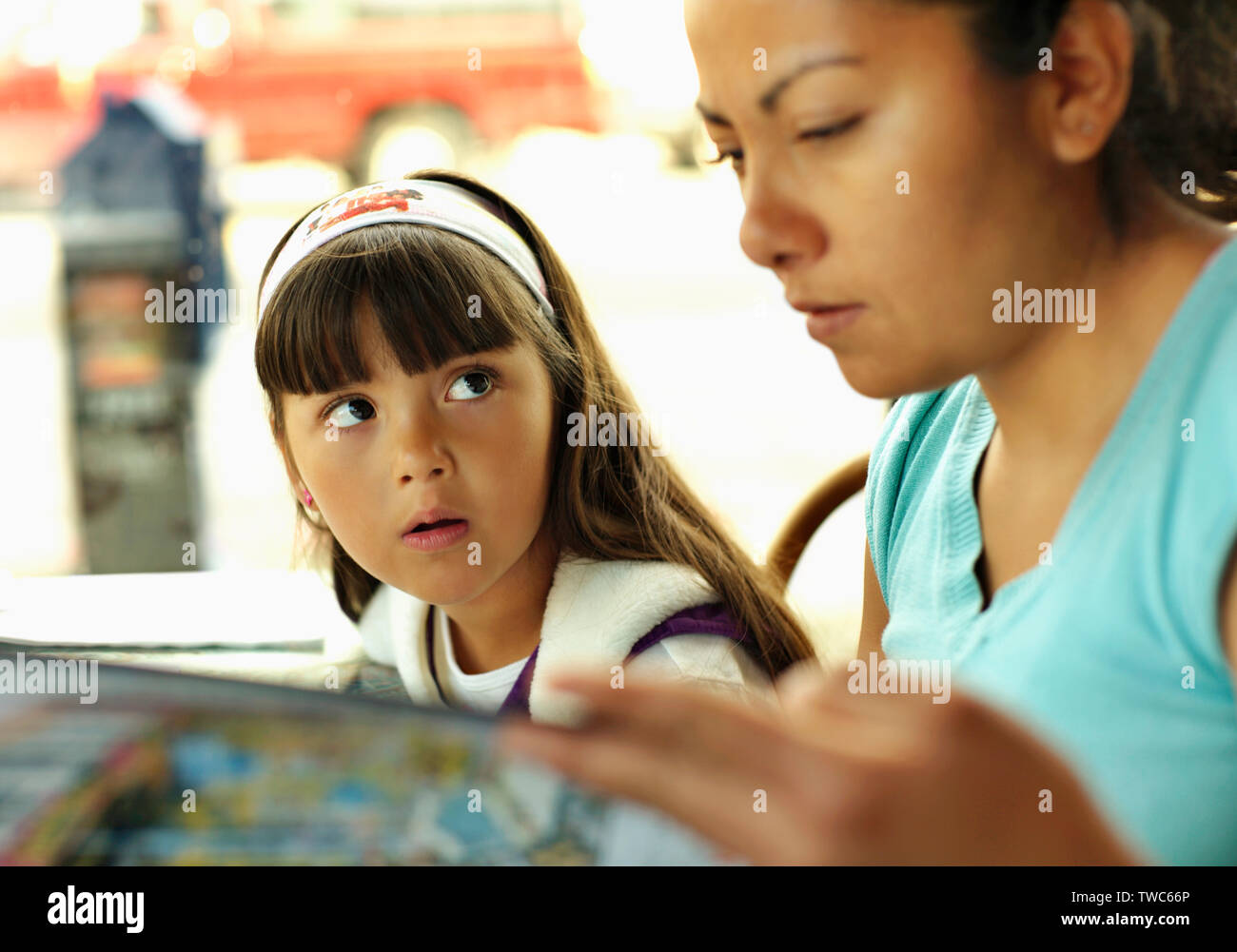 Young girl looks at her mother as she reads a restaurant menu. Stock Photo