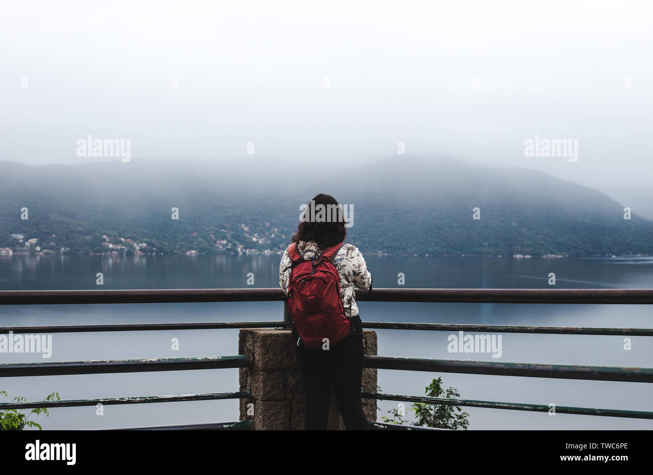 Travel girl backpacker young woman with red backpack at the edge of a misty mountain lake in Florianópolis, Brazil Stock Photo