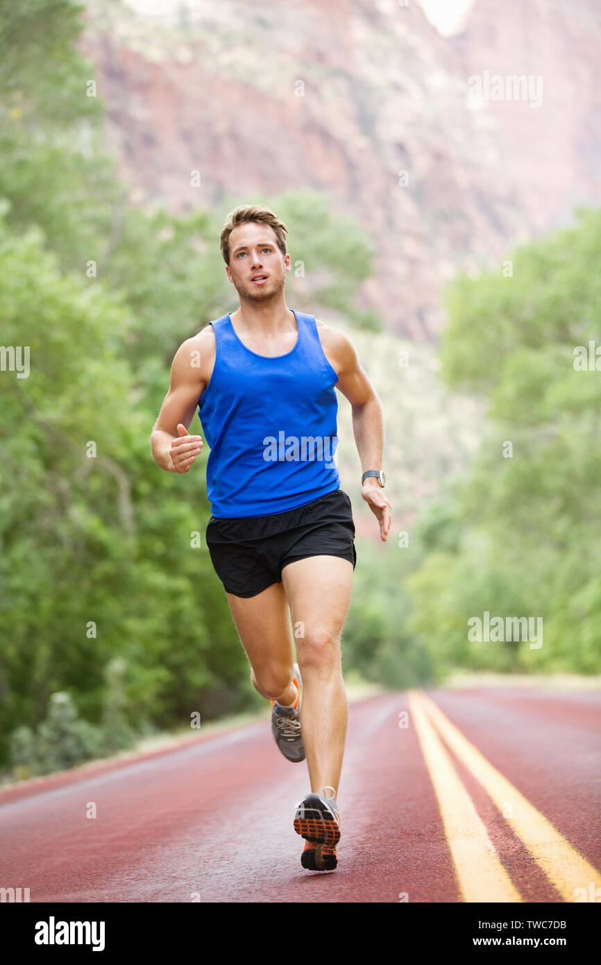Runner - running athlete man. Male sprinting during outdoors training for  marathon run. Athletic fit young sport fitness model in his twenties in  full body length on road outside in nature Stock