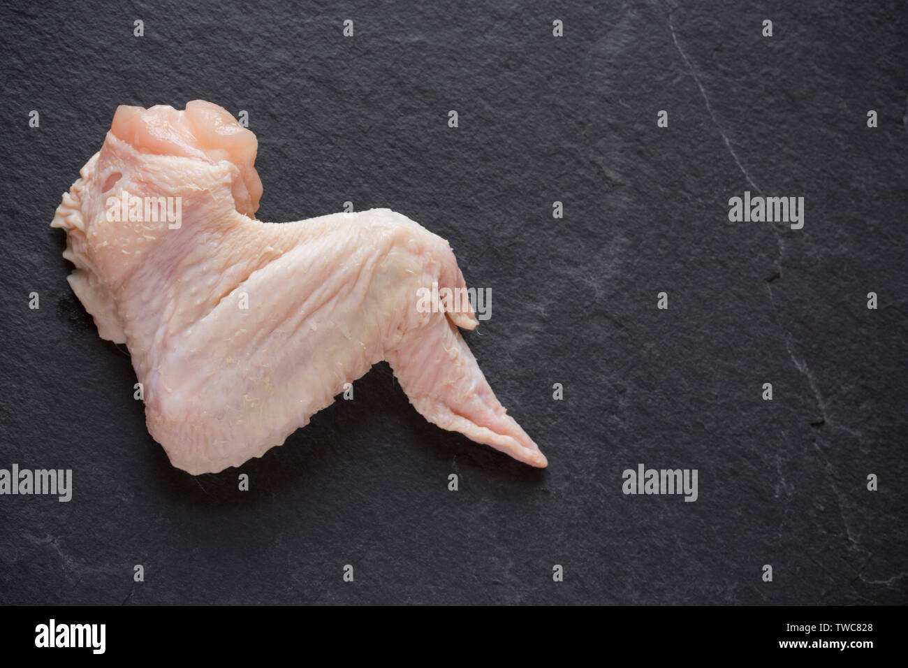 A single, raw, uncooked British chicken wing bought from a supermarket in the UK and photographed on a dark slate background. Dorset England UK GB Stock Photo