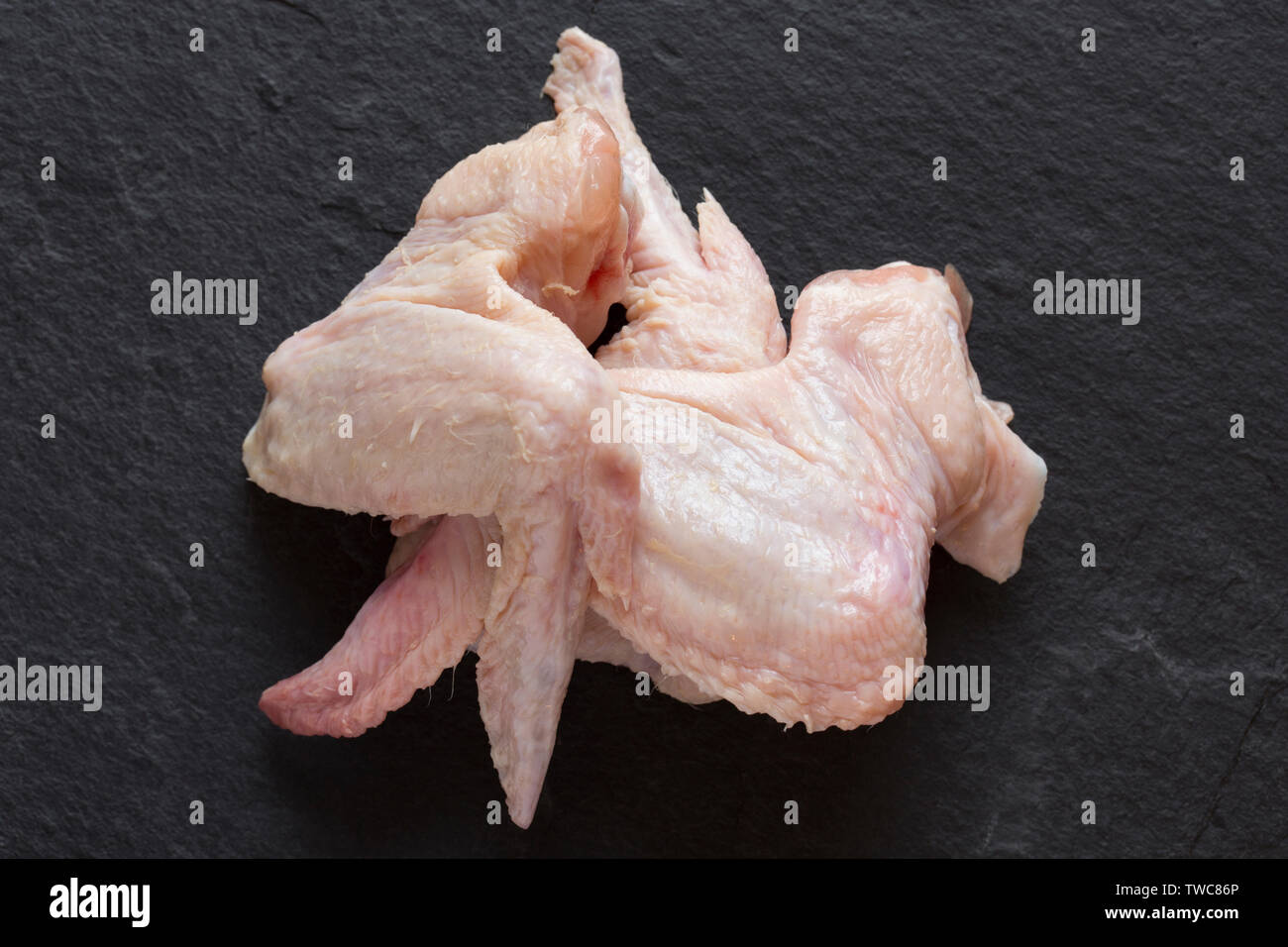 Three raw, uncooked British chicken wings bought from a supermarket in the UK and photographed on a dark slate background. Dorset England UK GB Stock Photo