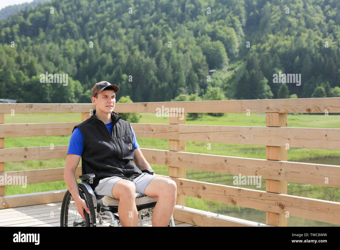 Disabled young man on a wheelchair on a wooden bridge path enjoying in nature Stock Photo