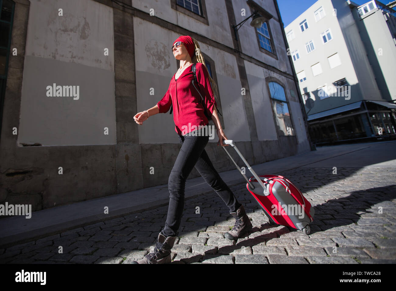 Woman with a red suitcase walking down the street of the city. Stock Photo