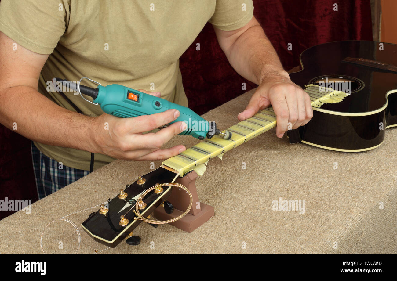 Musical instrument guitar repair and service - Worker polishing guitar neck frets dremel and paste GOI. Stock Photo