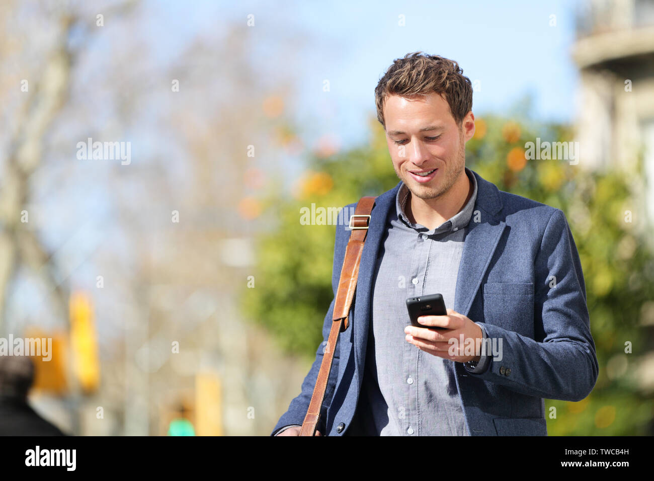 Young urban businessman professional on smartphone walking in street using app texting sms message on smartphone wearing jacket on Passeig de Gracia, Barcelona, Catalonia, Spain. Stock Photo