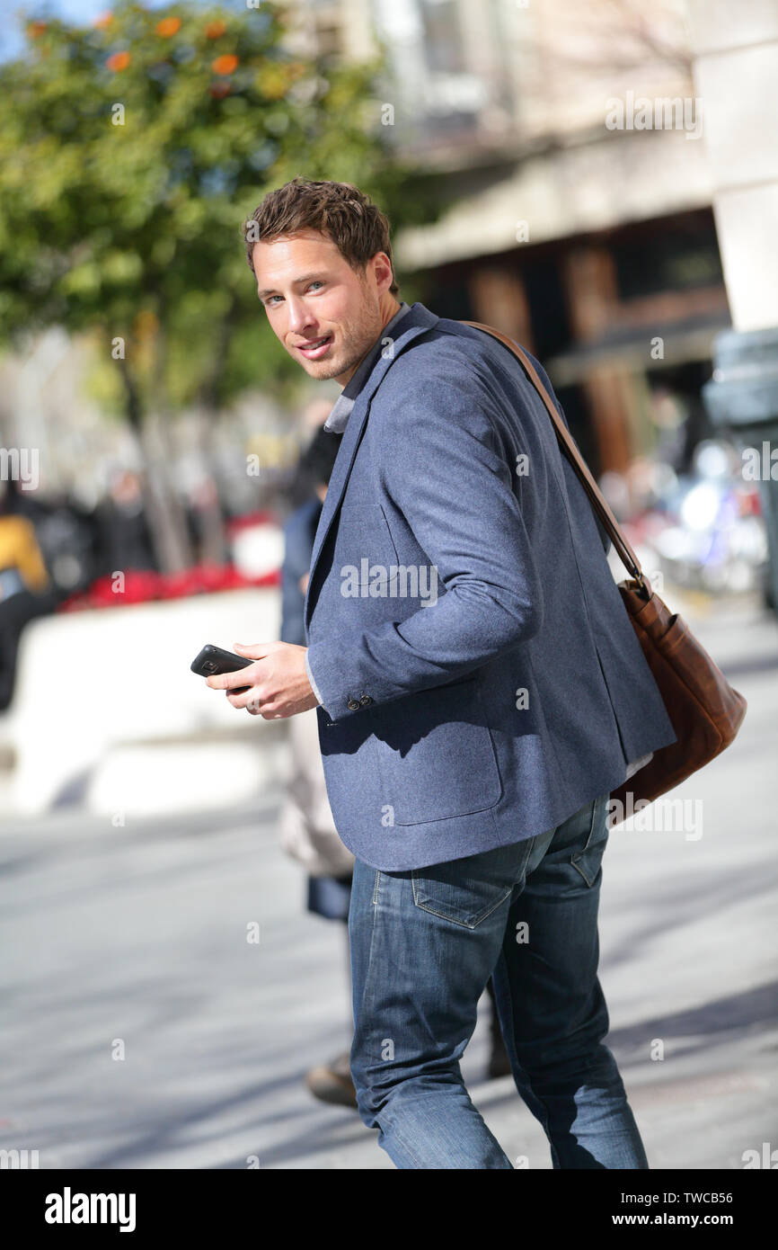 Young business man on smart phone walking in street with smartphone smiling wearing jacket on Passeig de Gracia, Barcelona, Catalonia, Spain. Stock Photo