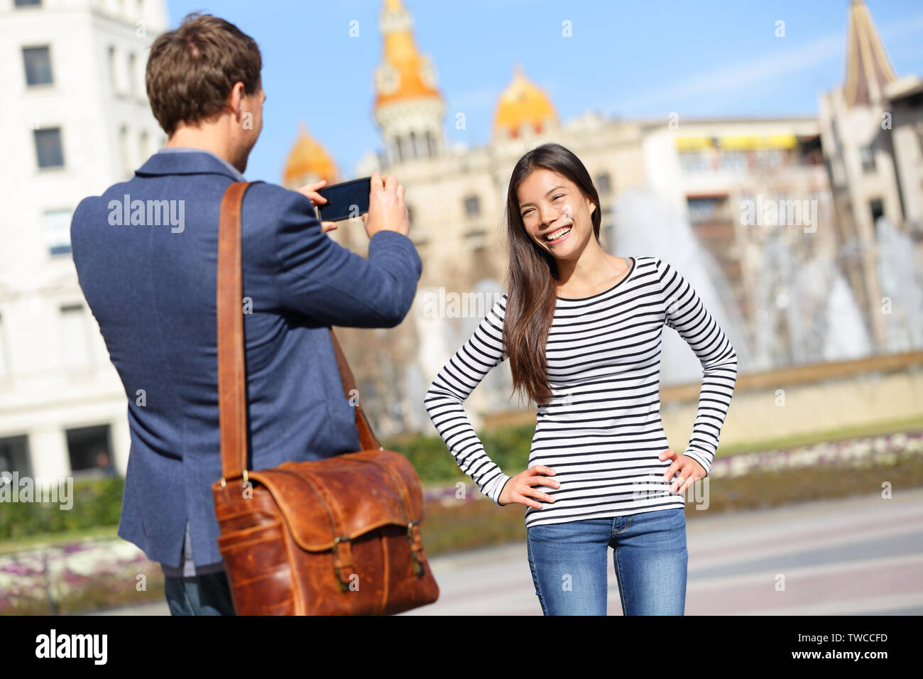 Tourists taking picture on travel in Barcelona. Happy urban young couple taking photo portrait with smart phone camera. Man and woman on Placa de Catalunya, Catalonia Square, Barcelona, Spain. Stock Photo