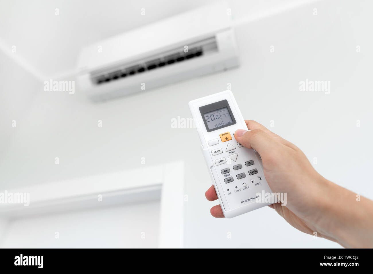 Air conditioner split on the wall inside the room. Man hand holding remote control Stock Photo