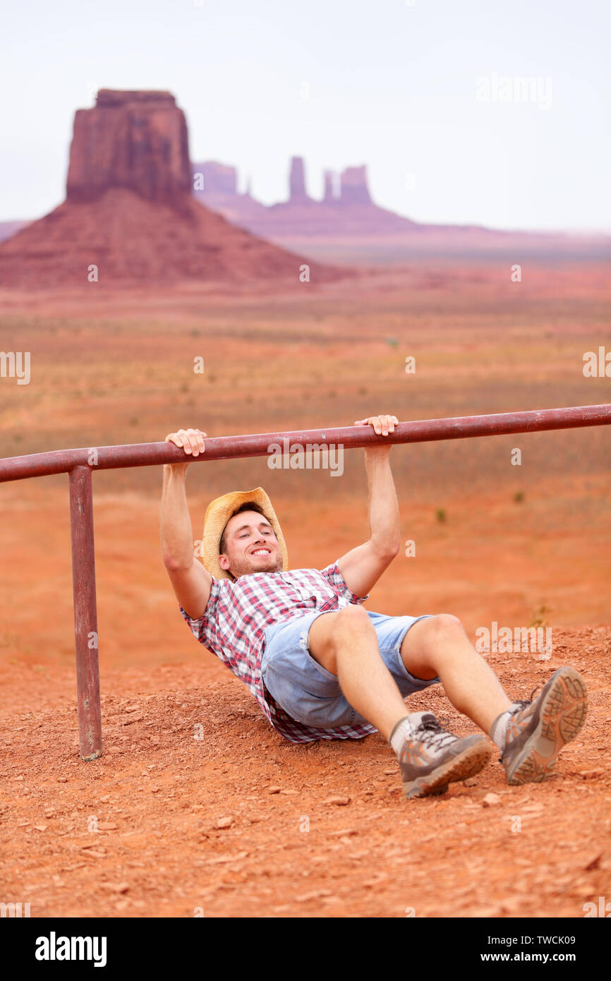 Fitness man training outdoors working out in amazing american landscape.  Cowboy man doing crossfit outside in nature wearing cowboy hat and casual  clothing during workout. Funny sport fitness concept Stock Photo -