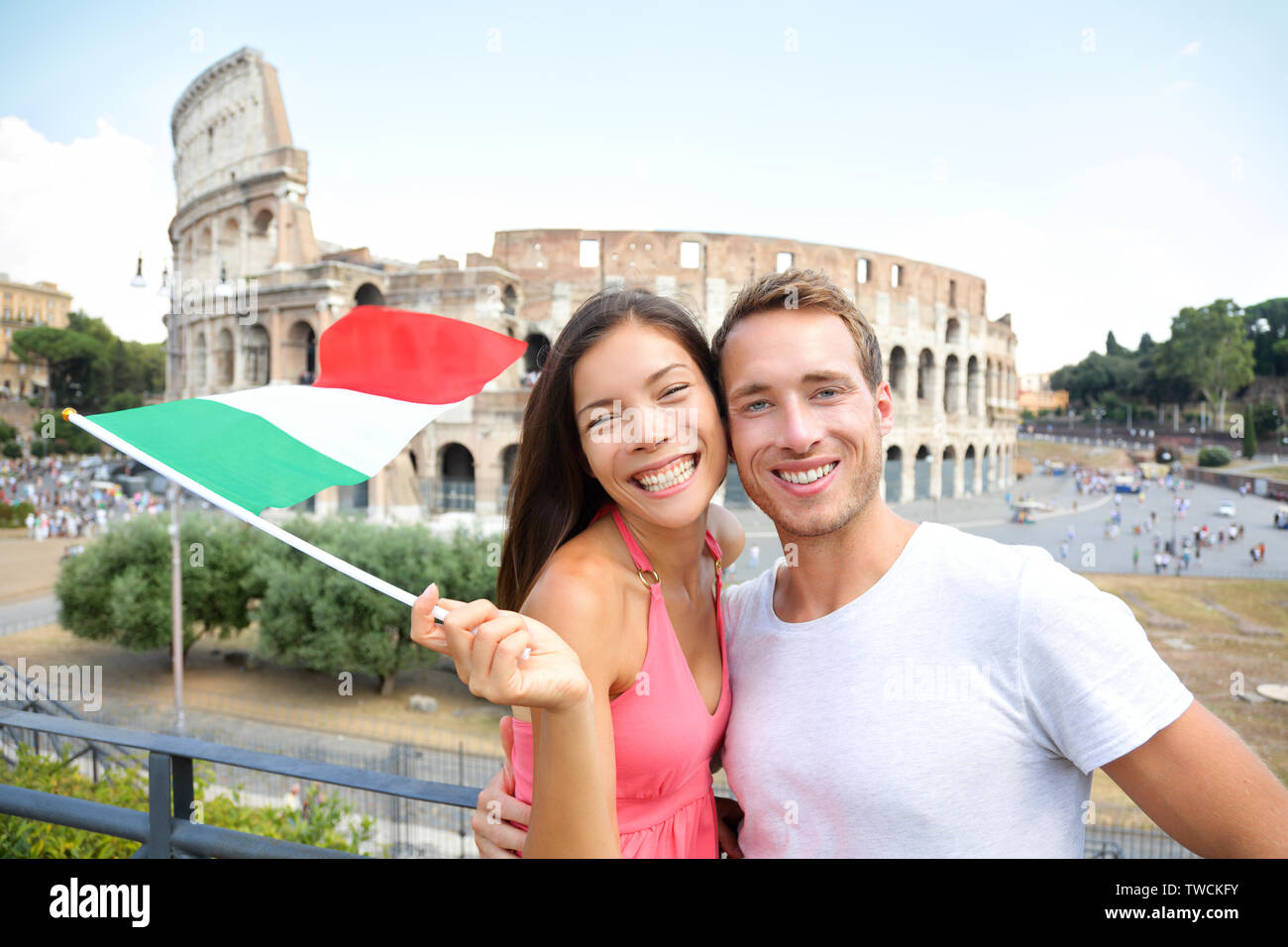 Italy travel couple with Italian flag by Colosseum embracing. Happy tourists lovers on honeymoon sightseeing having fun in front of Coliseum. Love and tourisn concept with multiracial couple. Stock Photo