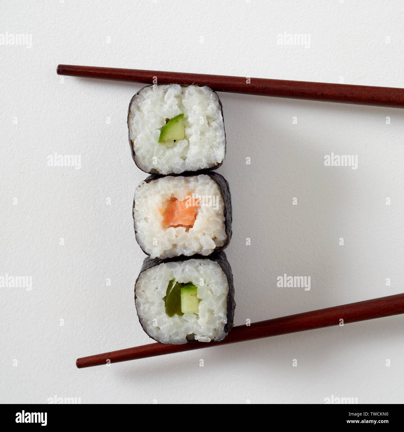 Food styling concept with three maki sushi rolls with nori seaweed, salmon and avocado pear placed between bamboo chopsticks on white with copy space Stock Photo