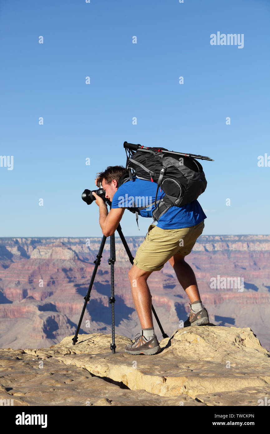 Nature landscape photographer in Grand Canyon taking picture photos with SLR camera and tripod during hike on south rim. Young man hiker enjoying landscape in Grand Canyon, Arizona, USA. Stock Photo