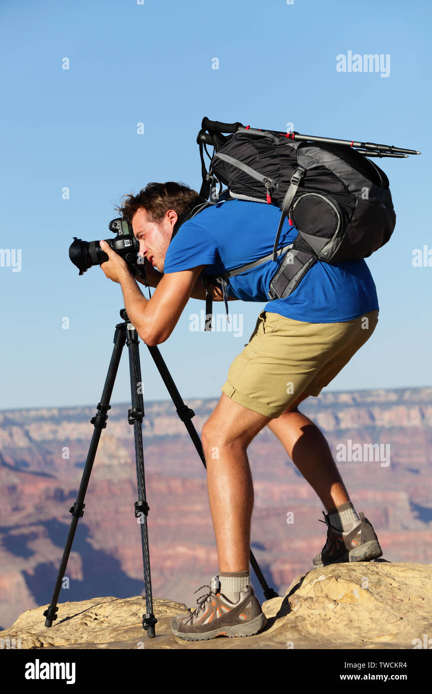 Photographer in Landscape nature in Grand Canyon taking picture photos with SLR camera and tripod during hike on south rim. Young man hiker enjoying landscape in Grand Canyon, Arizona, USA. Stock Photo