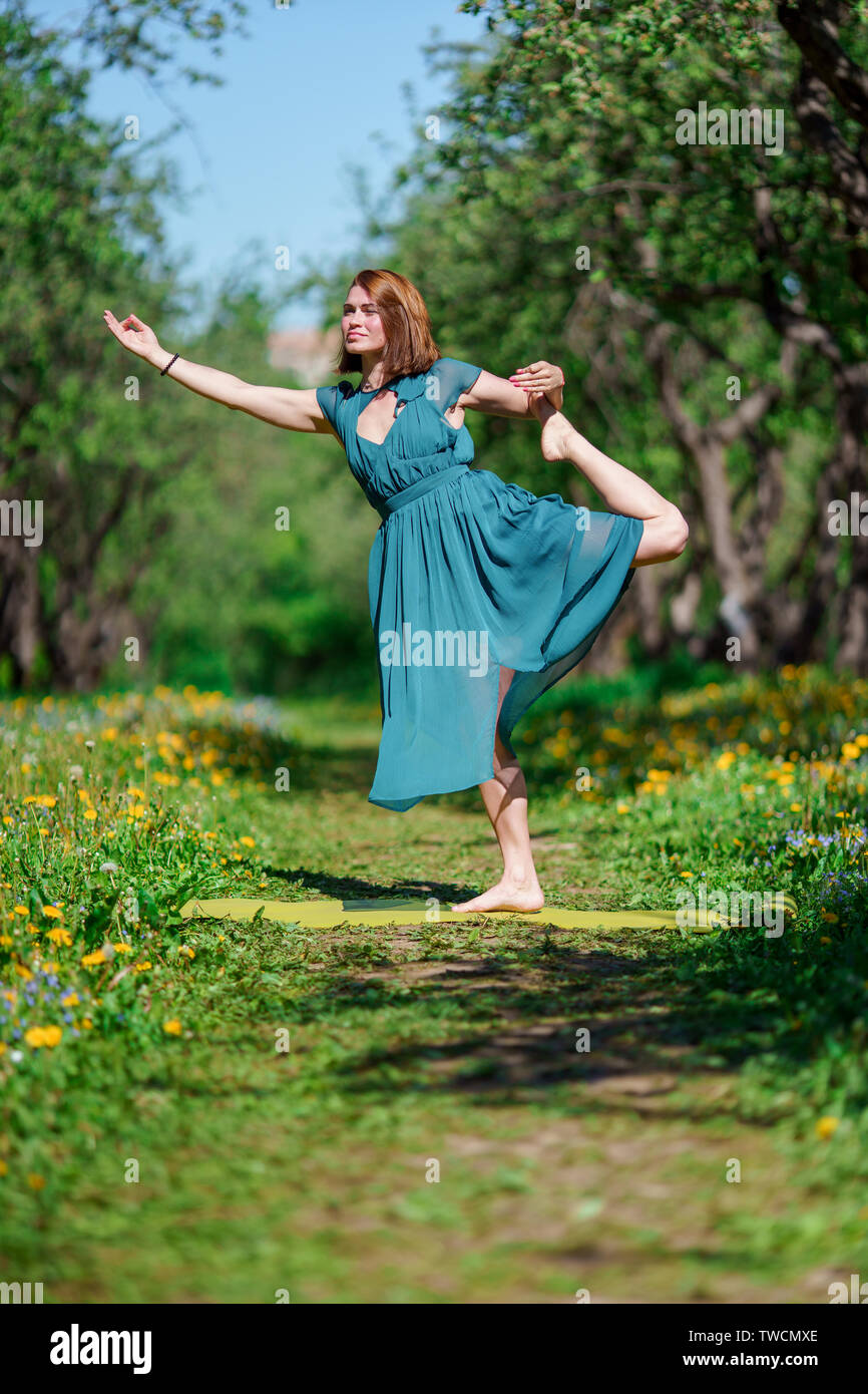 Photo of young woman in long green dress doing yoga in forest Stock Photo -  Alamy