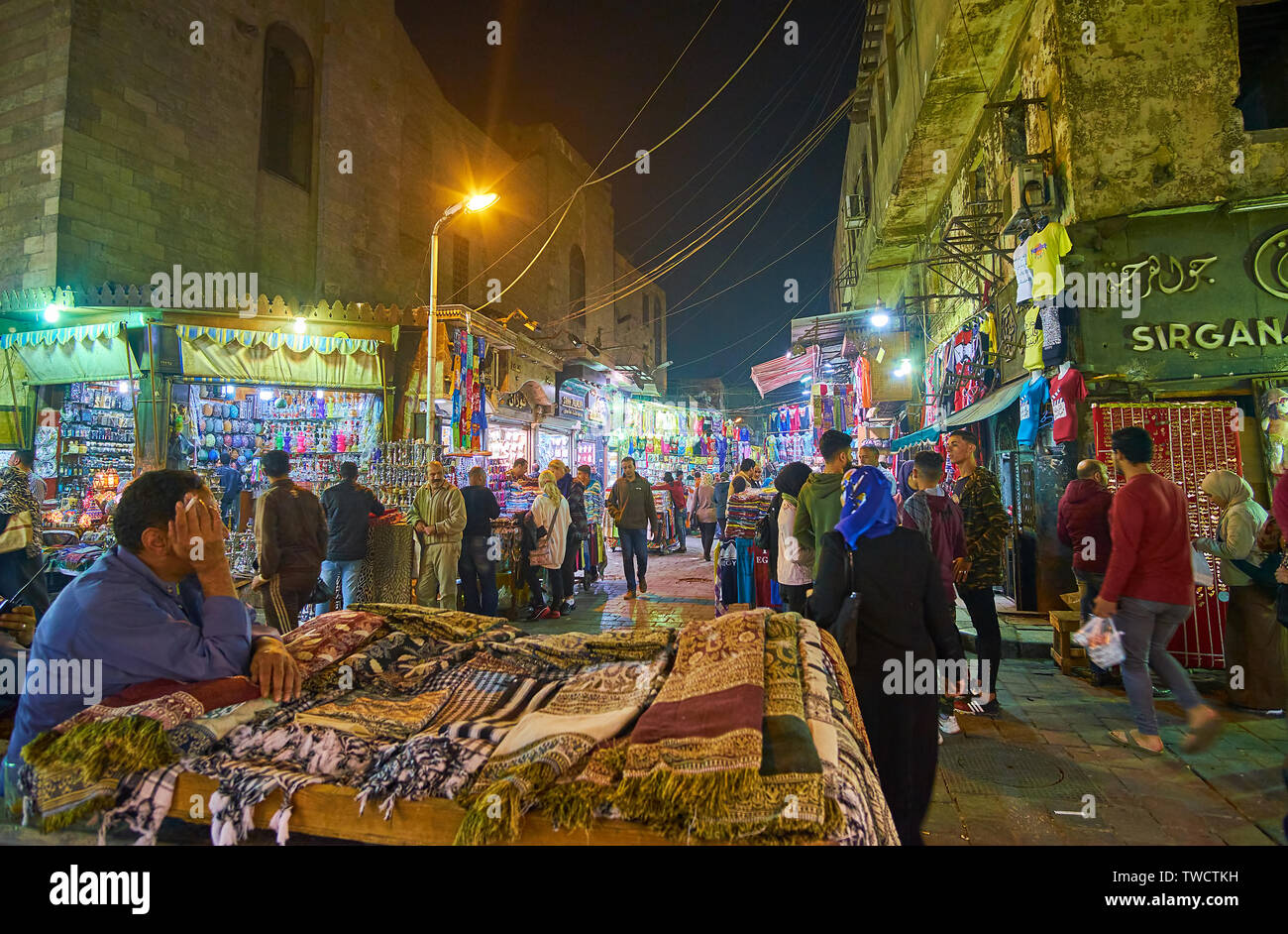 CAIRO, EGYPT - DECEMBER 22, 2017: The crowded evening street of Khan EL Khalili market with multiple illuminated stores and the traditional scarfs' st Stock Photo
