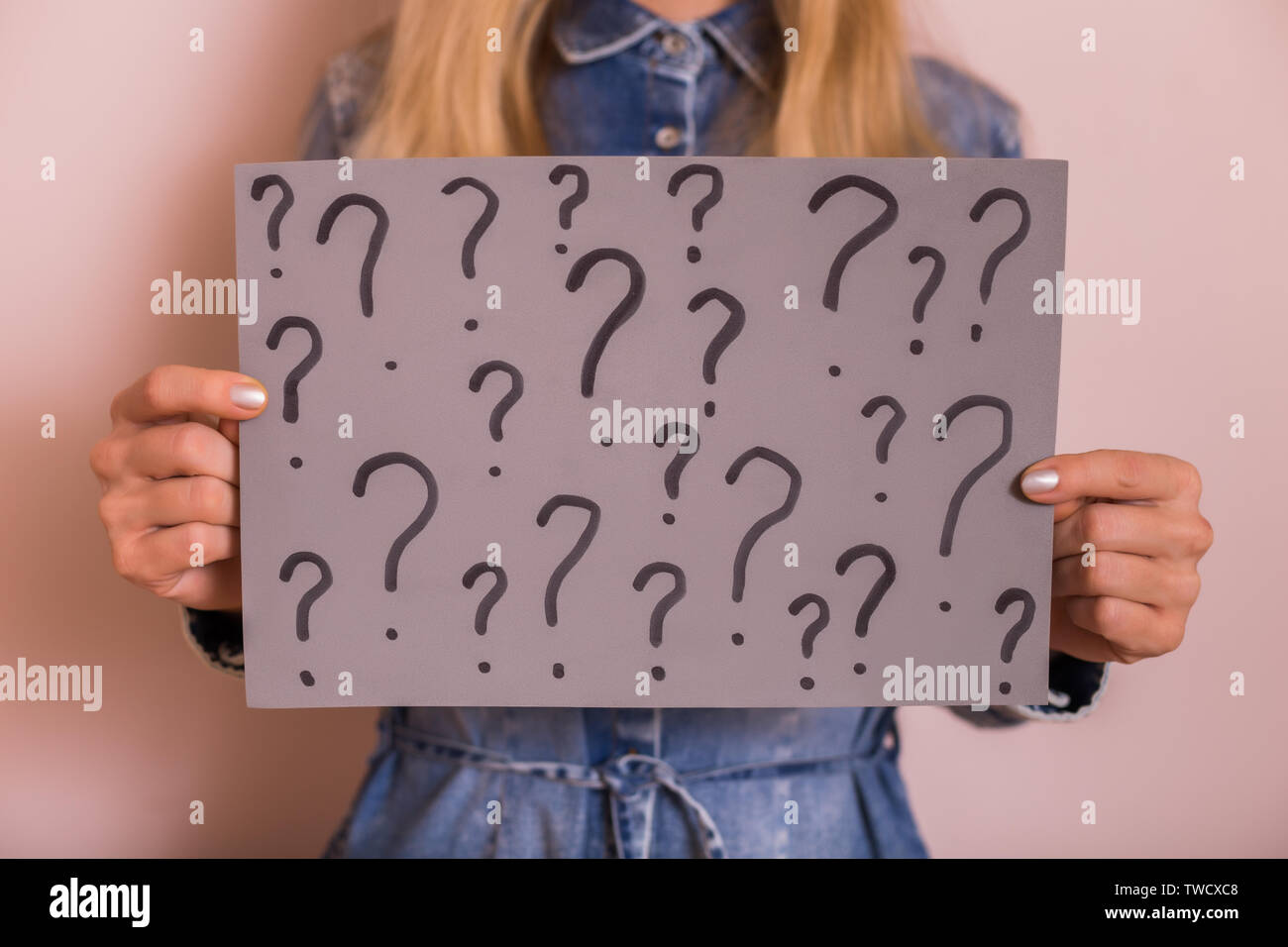 Woman holding paper with question marks while standing in front of the wall. Stock Photo