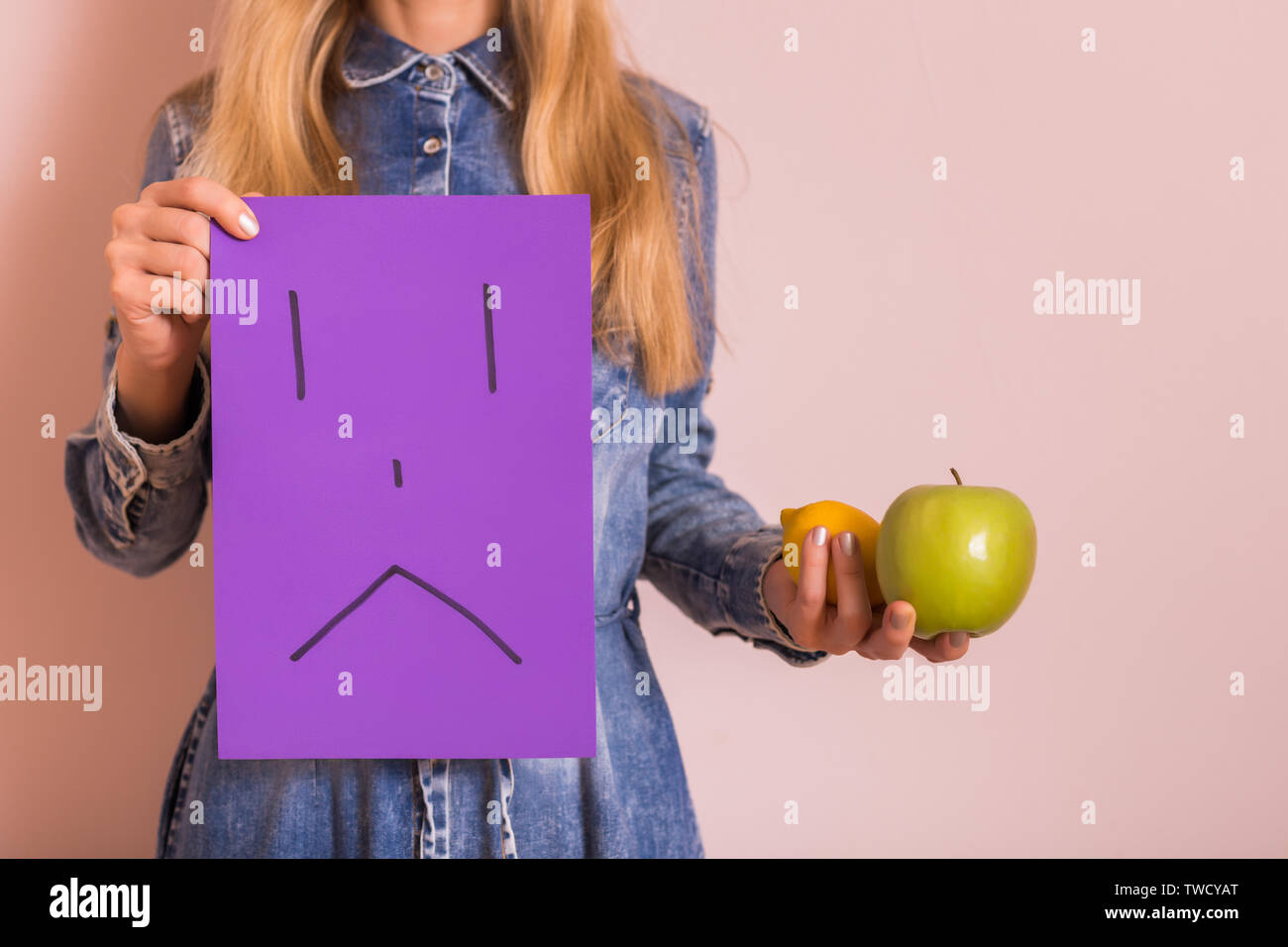 woman-holding-fruit-and-sad-face-on-paper-while-standing-in-front-of