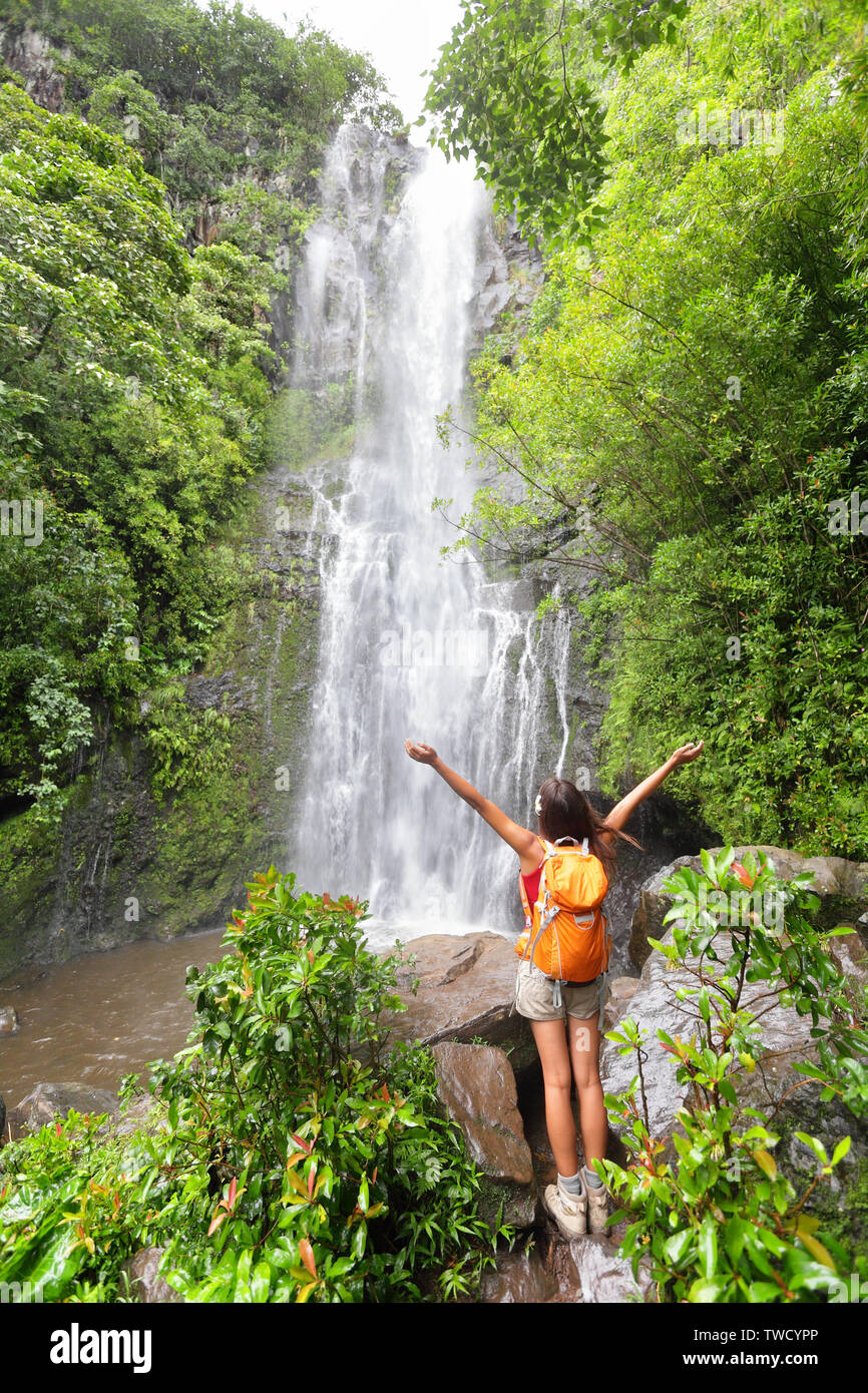 Happy hiker - Hawaii tourists hiking by waterfall. Woman cheering during travel on the road to Hana on Maui, Hawaii. Ecotourism concept image with happy female hiker. Stock Photo
