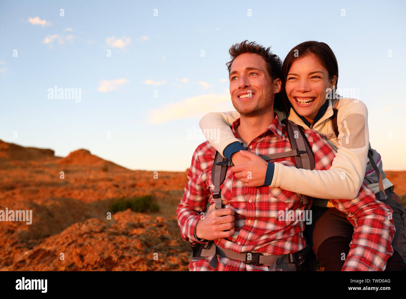 Happy couple active lifestyle hiking enjoying outdoors activity. Smiling laughing young lovers embracing looking at sunset during hike. Cheerful interracial couple, Asian woman, Caucasian man. Stock Photo