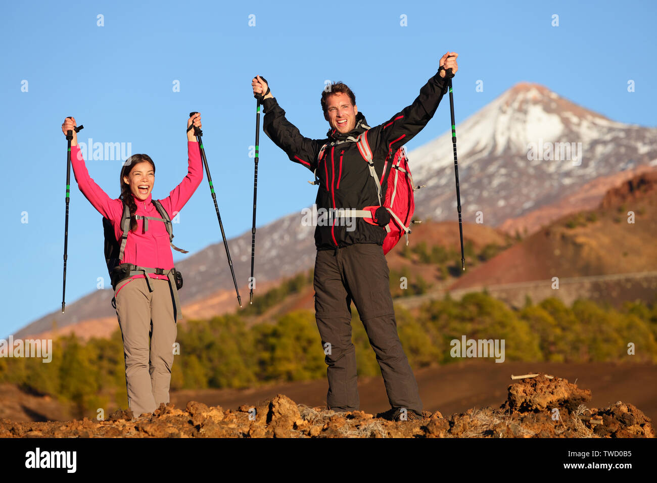 Success winning celebrating hiking people at top. Cheering hiker couple enjoying freedom on hike with arms raised in mountain landscape. Woman and man on volcano Teide, Tenerife, Canary Islands, Spain Stock Photo