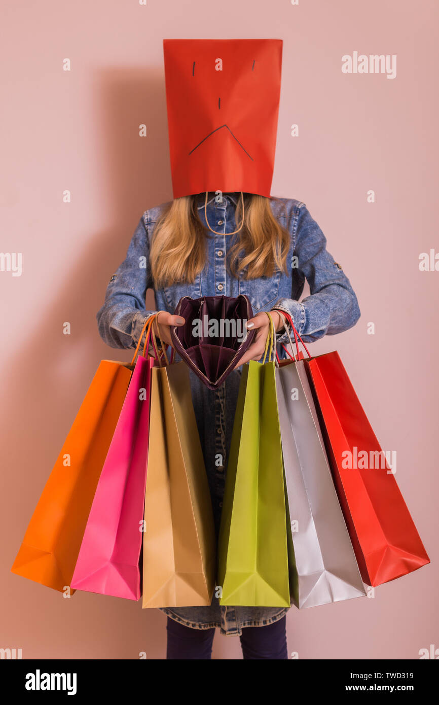 Sad woman holding shopping bags and empty wallet while standing in ...