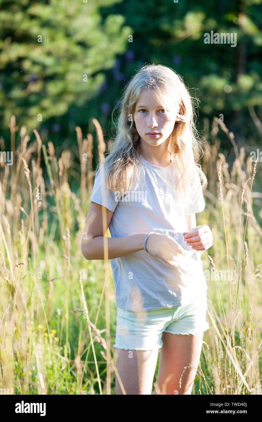 teen blonde white girl standing on green summer outdoor meadow Stock Photo