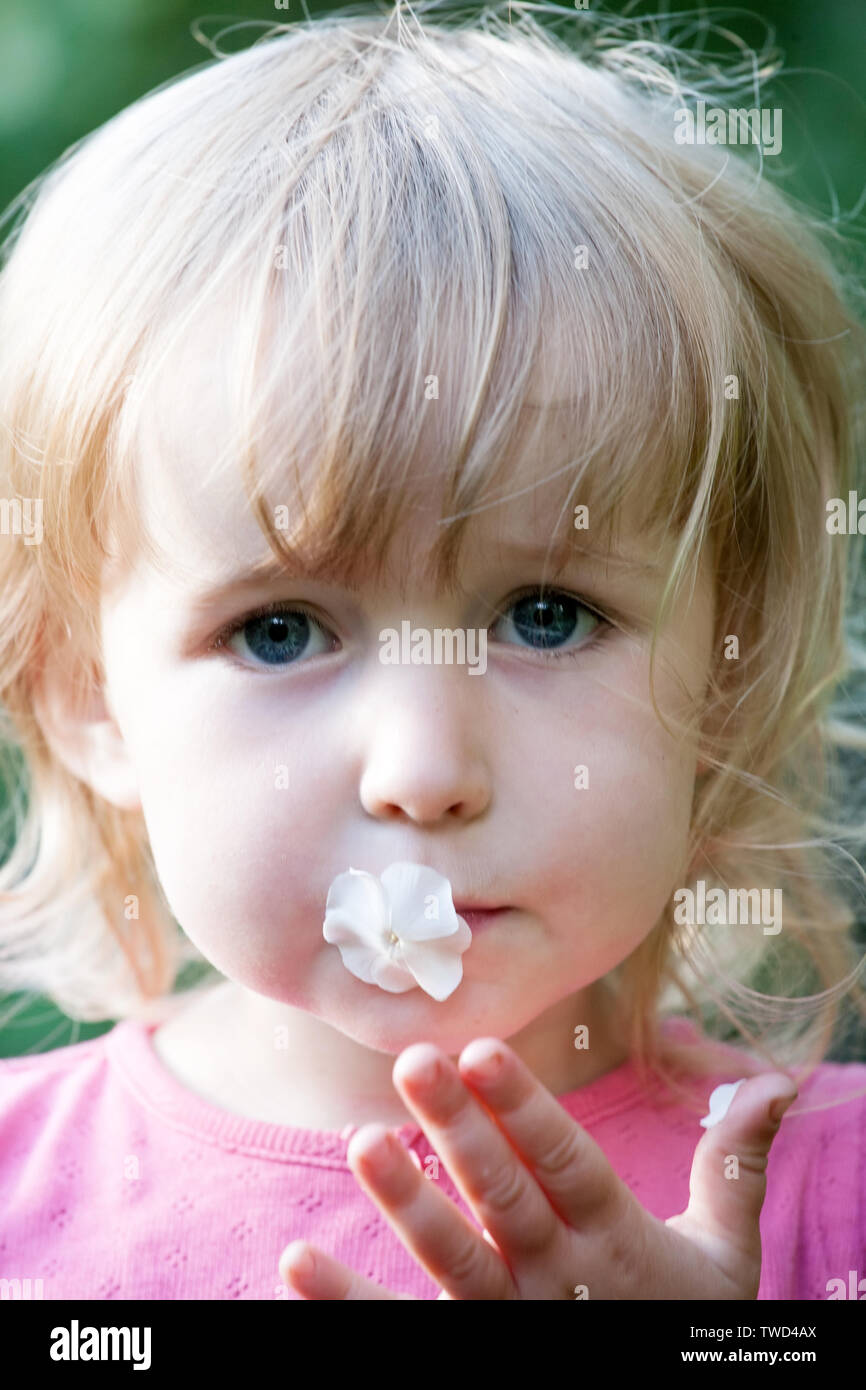 two years old caucasian girl with small white flower in the mouth Stock Photo