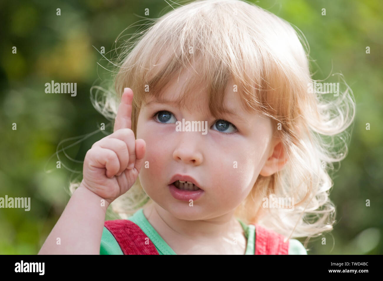 little child face and index finger pointing up closeup view on green outdoor background Stock Photo