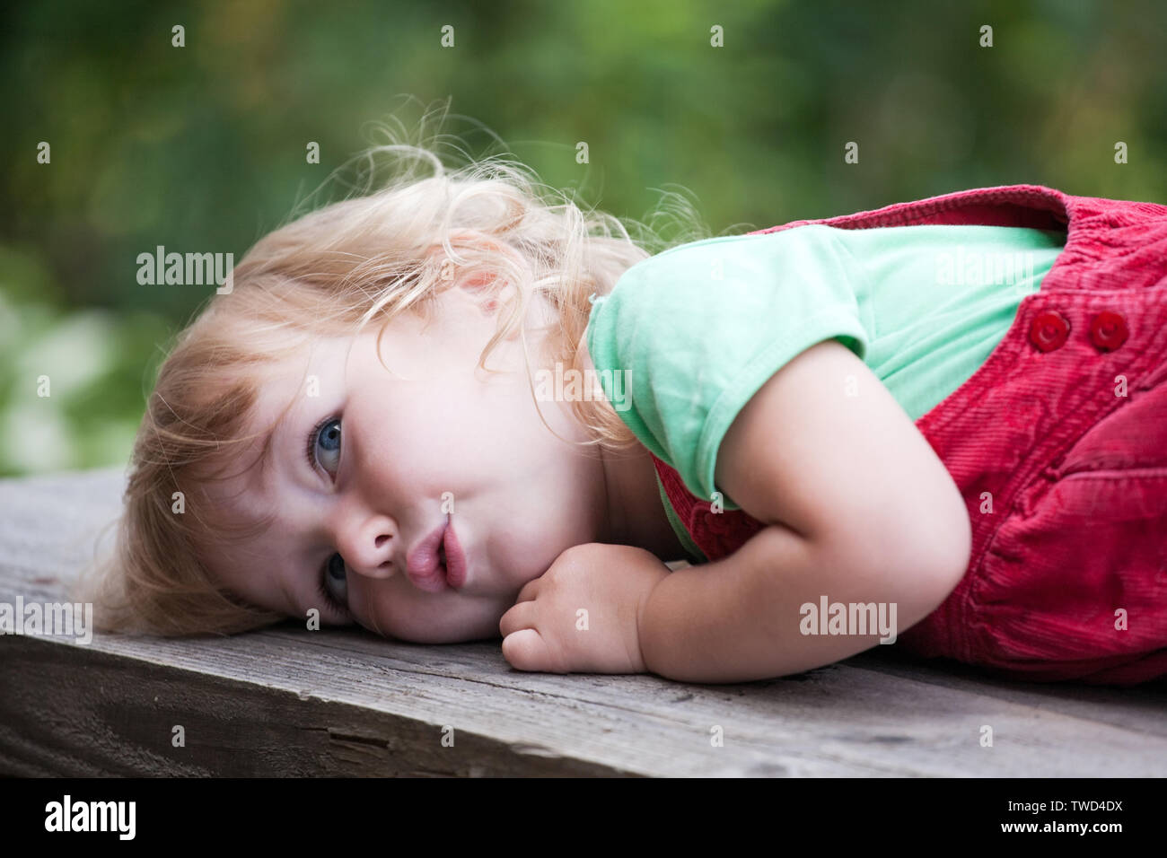 cute pensive kid girl lying on outdoor wooden bench Stock Photo
